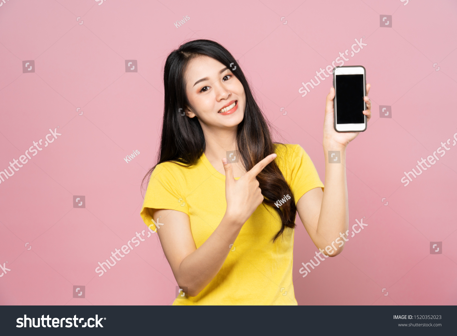 Portrait of Asian beautiful young woman holding smartphone and pointing finger on mobile phone with smile face. The girl standing and looking at camera in studio. Advertisement & presentation concept. #1520352023