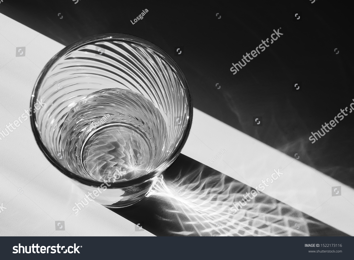 A glass of water on the windowsill in sunny weather. The light is refracted through the water and the edge of the vessel and creates a fantastic kyaroskuro pattern. Close up, shot from above. 

 #1522173116