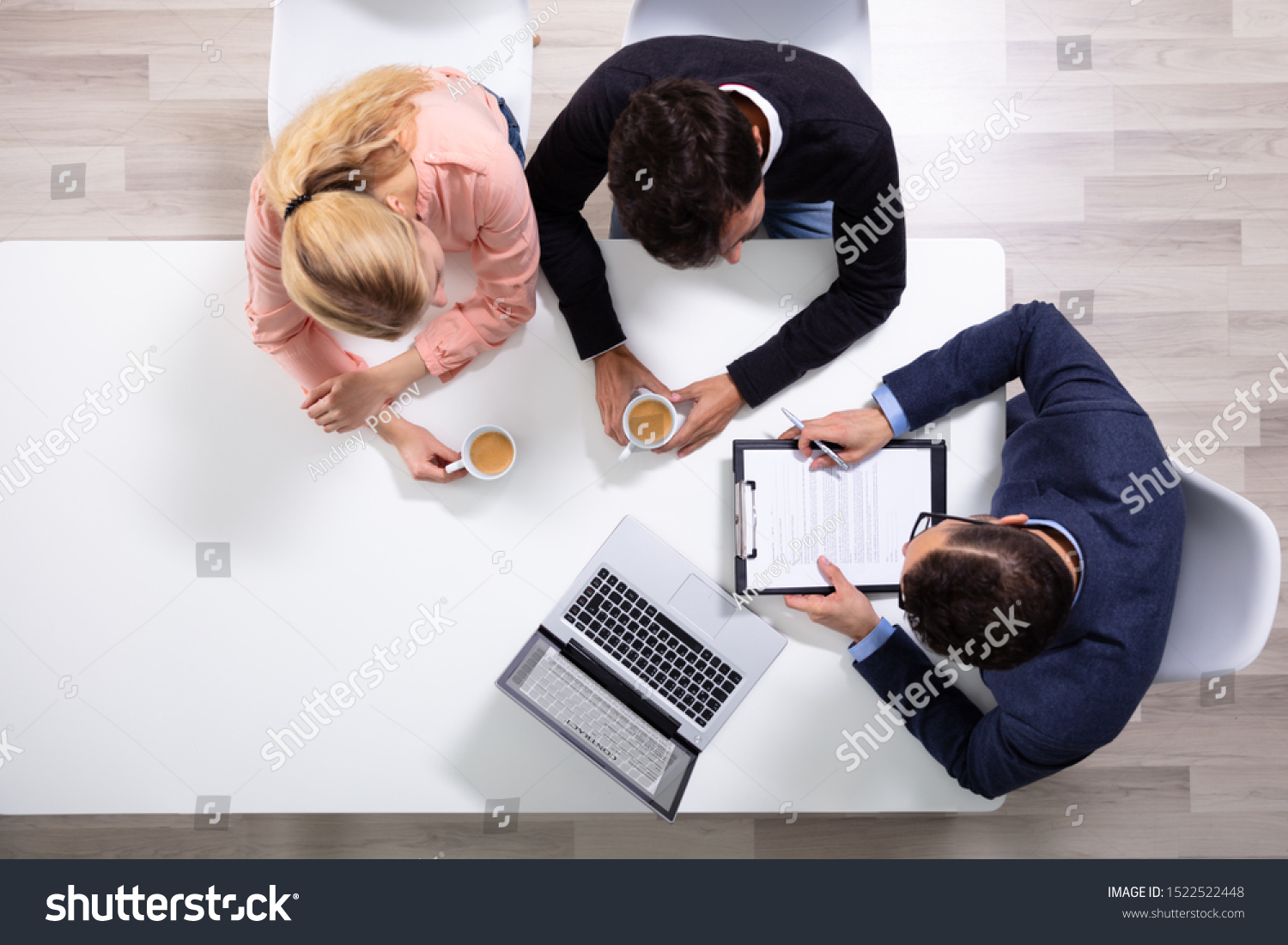 Happy Young Couple Consulting Male Friendly Financial Advisor With Coffee Cups At Office Desk #1522522448