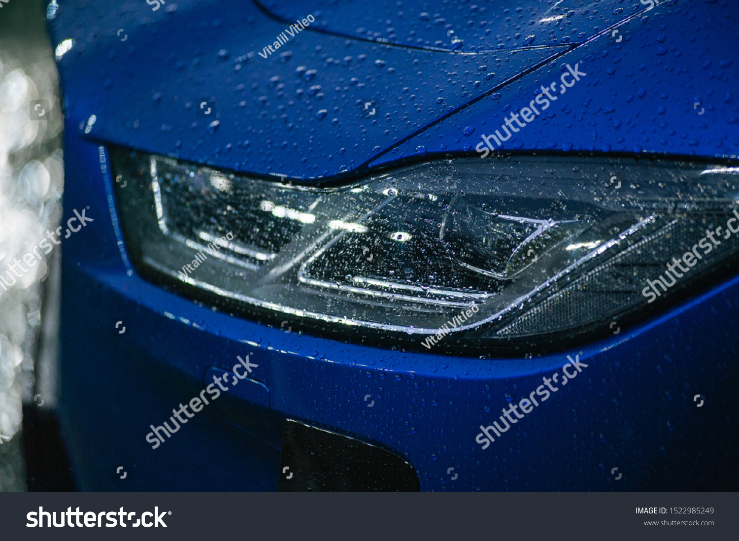 Headlight detail of blue car with water drop after car wash. Close up of headlamp. Side view shot from side of vehicle. Lens and reflector design. Detailing concept. #1522985249