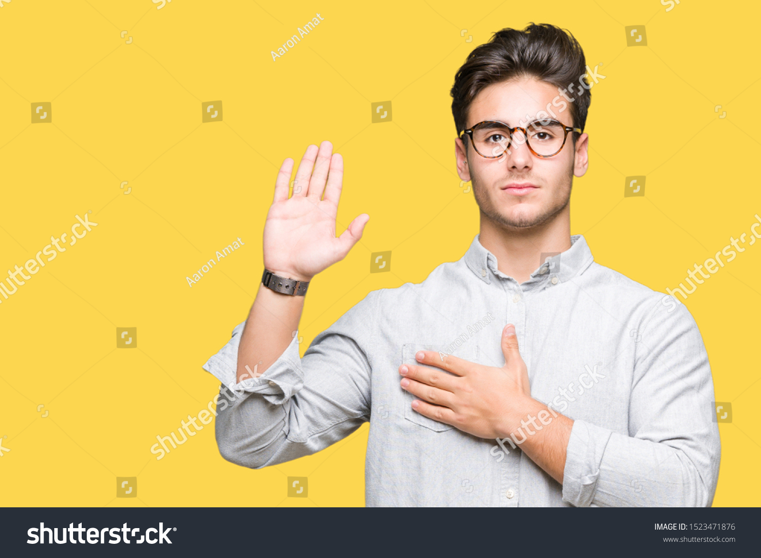 Young handsome man wearing glasses over isolated background Swearing with hand on chest and open palm, making a loyalty promise oath #1523471876