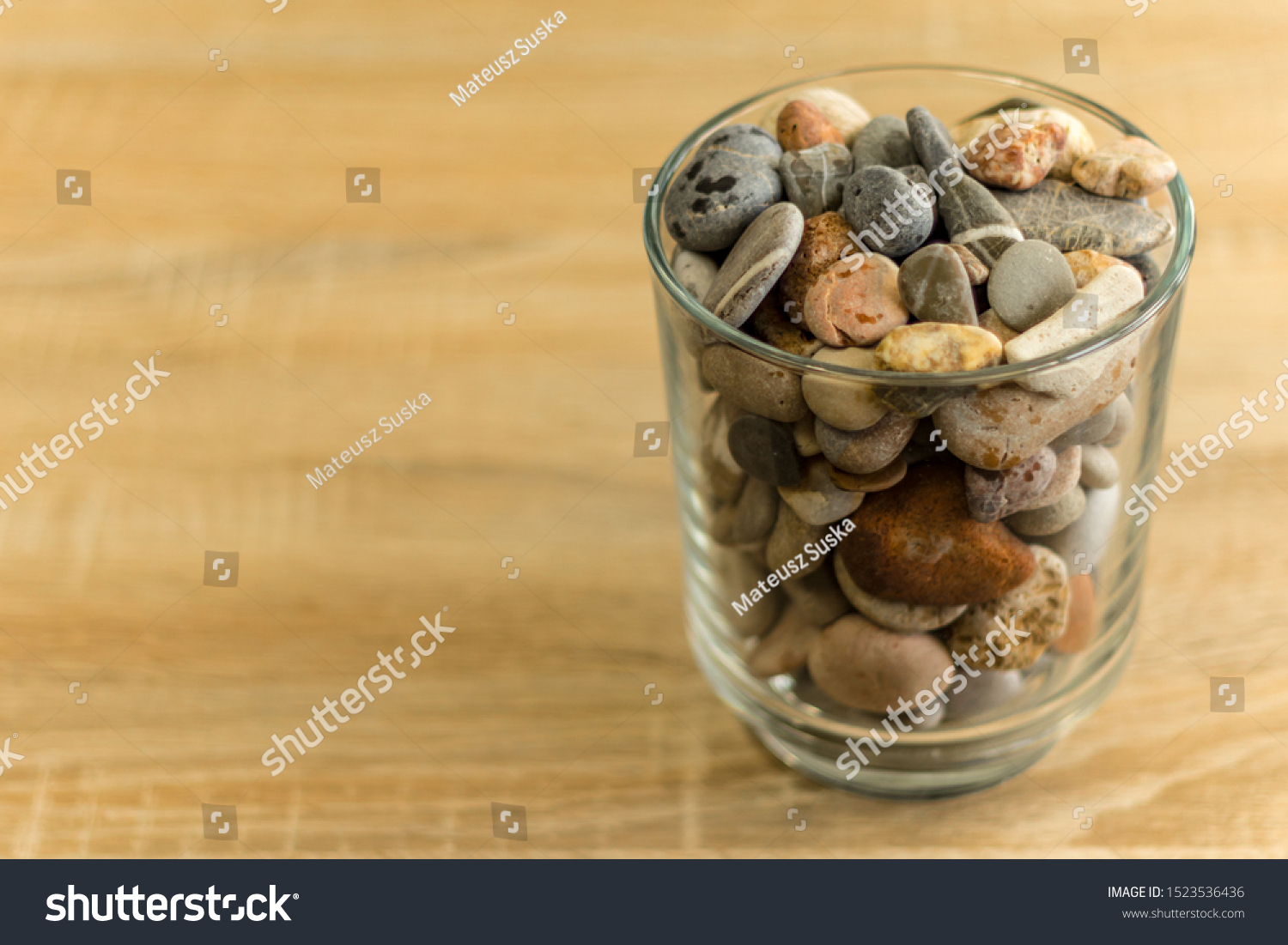 Small sea stones in a glass vessel. The idea of decorating the house with small rocks in a jar on a wooden blurred background. #1523536436