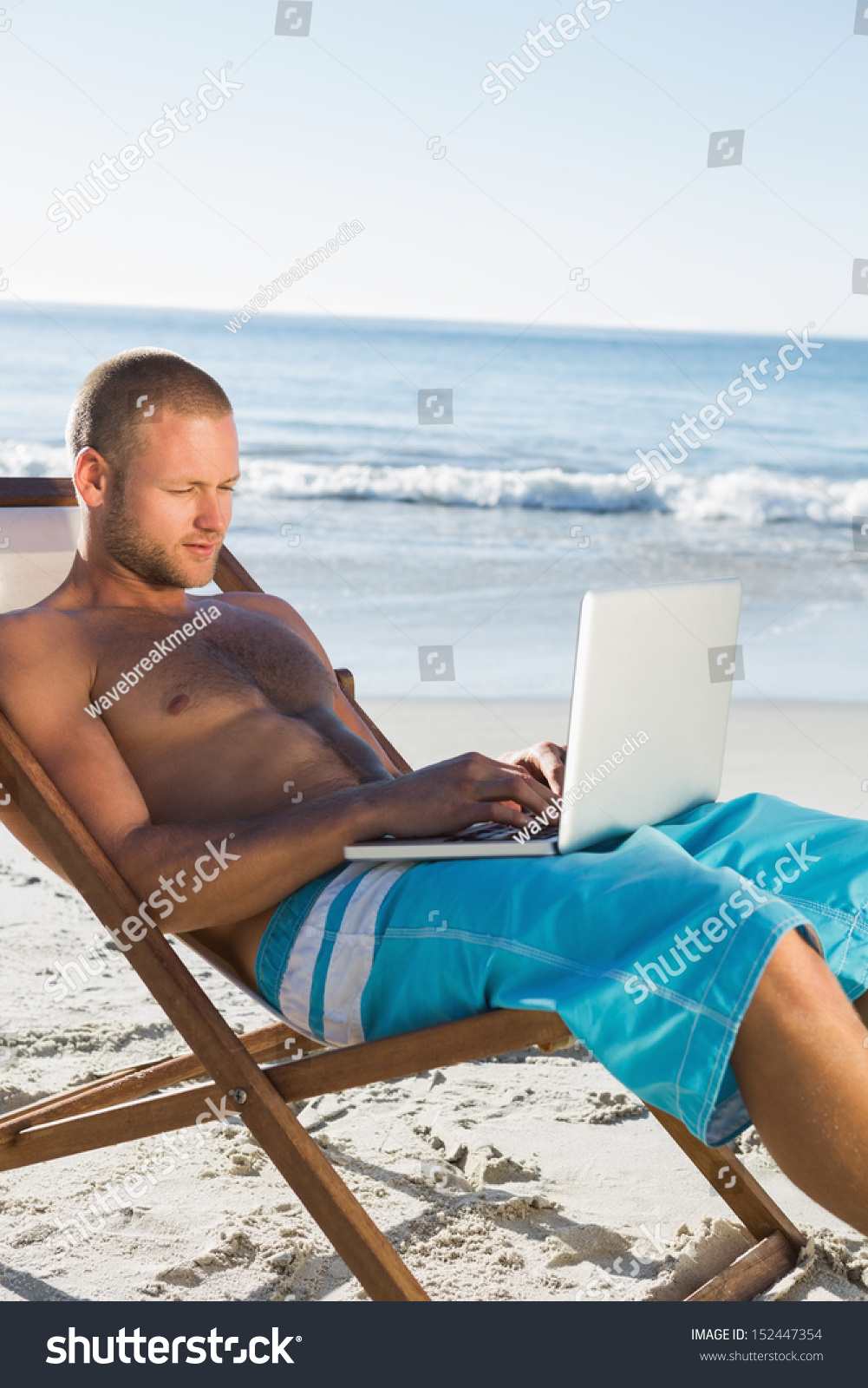 Handsome man on the beach using his laptop sitting on his deck chair #152447354