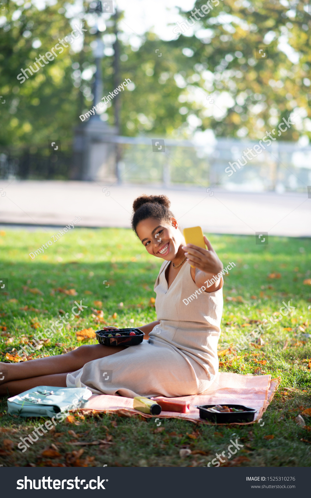 Cheerful woman. Cheerful woman holding yellow smartphone while making selfie having little picnic #1525310276
