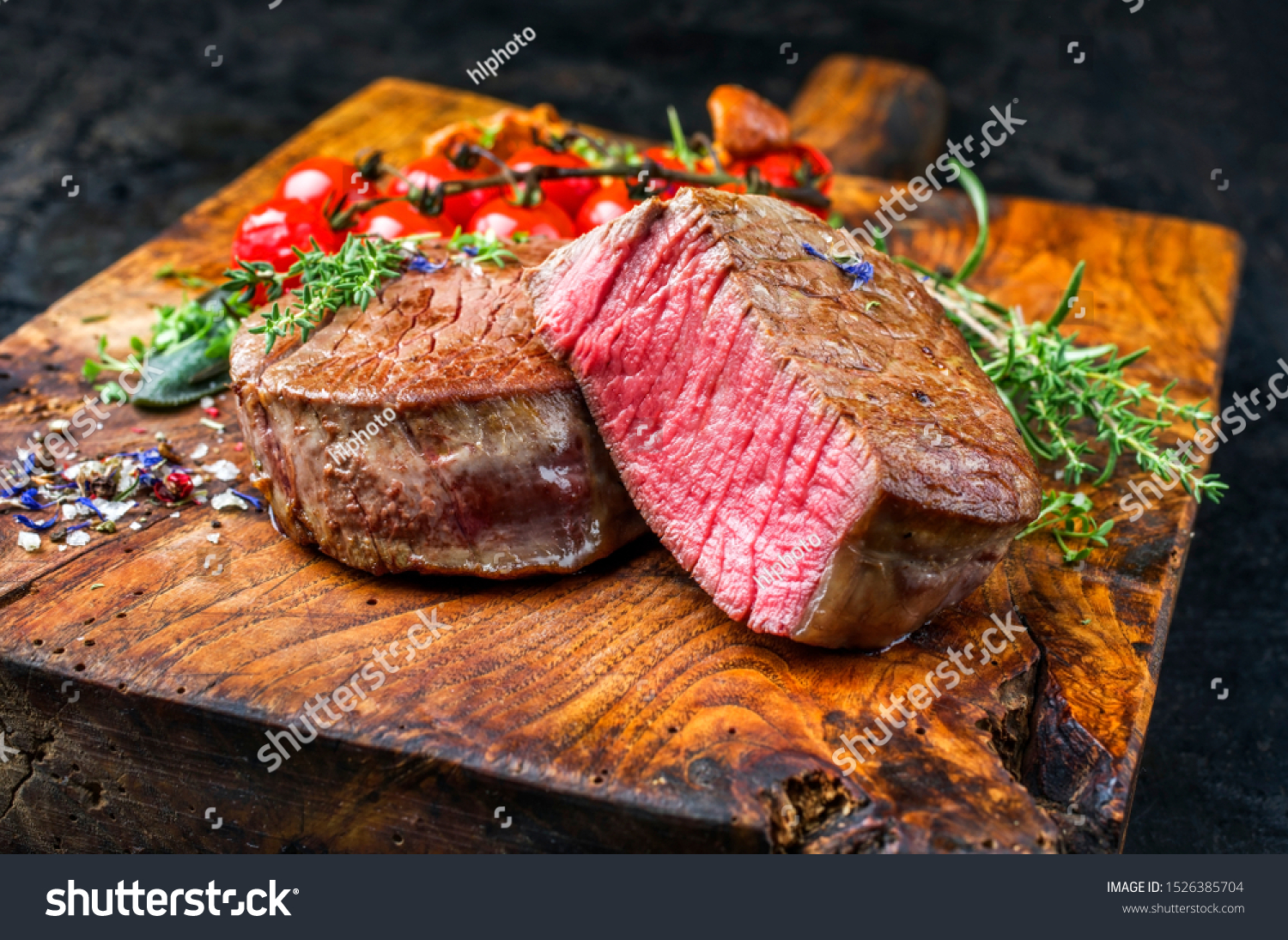 Fried dry aged beef fillet medallion steak natural with tomatoes and herbs as closeup on a wooden cutting board  #1526385704