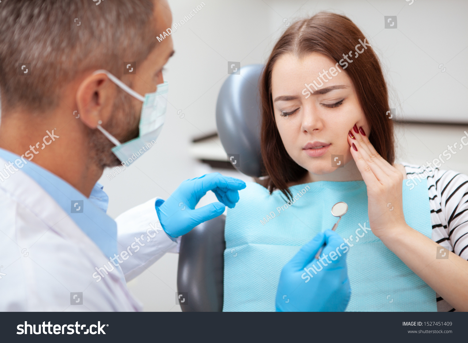Young woman having toothache, sitting in a dental chair at the clinic. Female patient with terrible toothache visiting dentist #1527451409