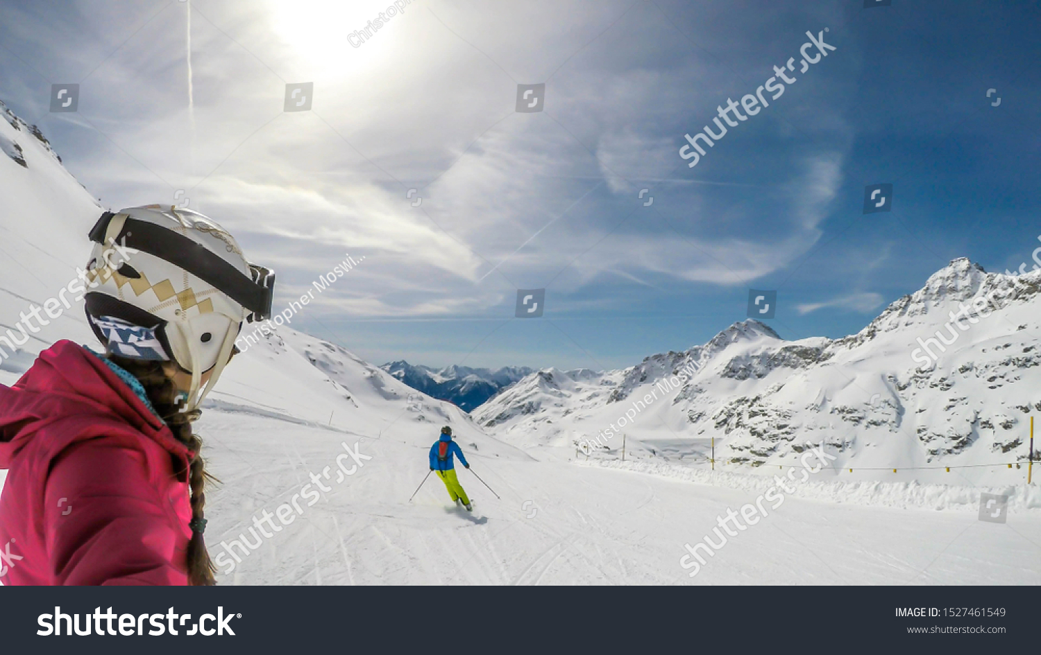 A snowboarding girl and skiing man going down the slope in Mölltaler Gletscher, Austria. Perfectly groomed slopes. High mountains surrounding the couple. They wear helm for the protection. Active life #1527461549