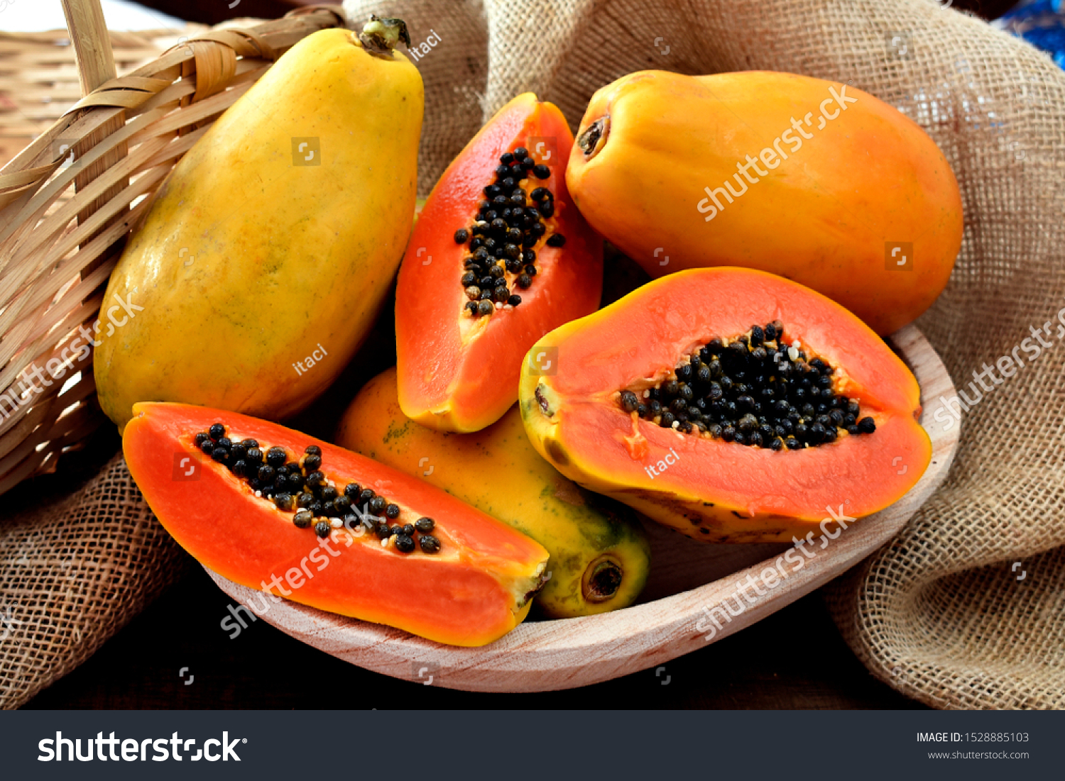 The papaya fruits in a wooden pot and a straw basket and rustic fabric at the background #1528885103