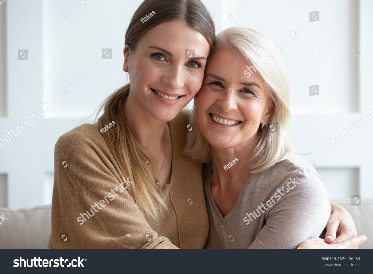 Close up image aged mother adult daughter sitting on couch indoors smiling looking posing for camera hugging feels happy spend time together, concept of love relative people, multi-generational family #1529466284