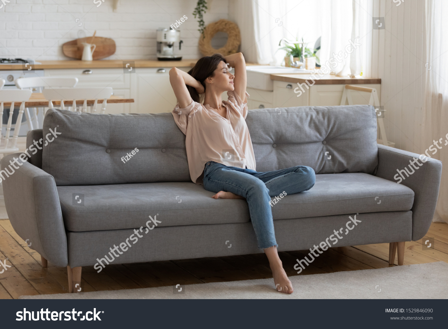 Calm serene young woman relaxing on comfortable couch at home with closed eyes and hands behind head, satisfied girl stretching on sofa, daydreaming and meditating in cozy living room #1529846090