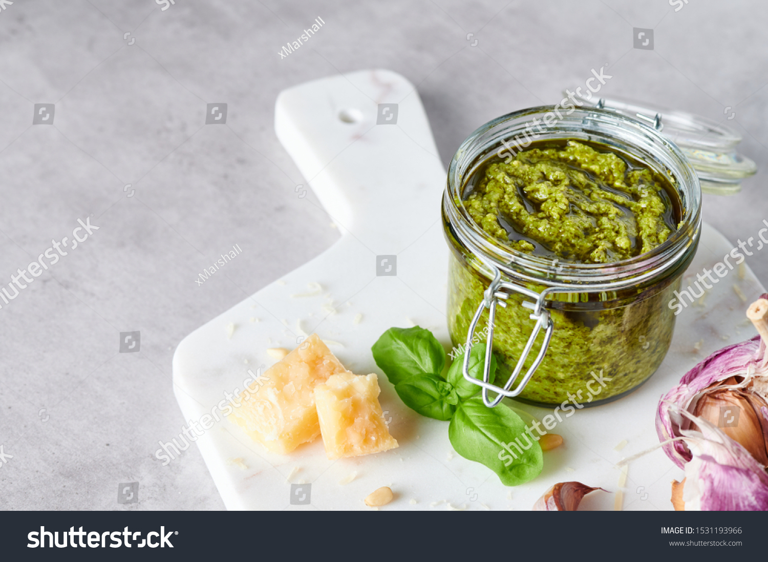 Pesto sauce or pesto genovese in a glass jar with pine nuts, parmesan, basil, oil and garlic on white marble cutting board. Copy space. #1531193966