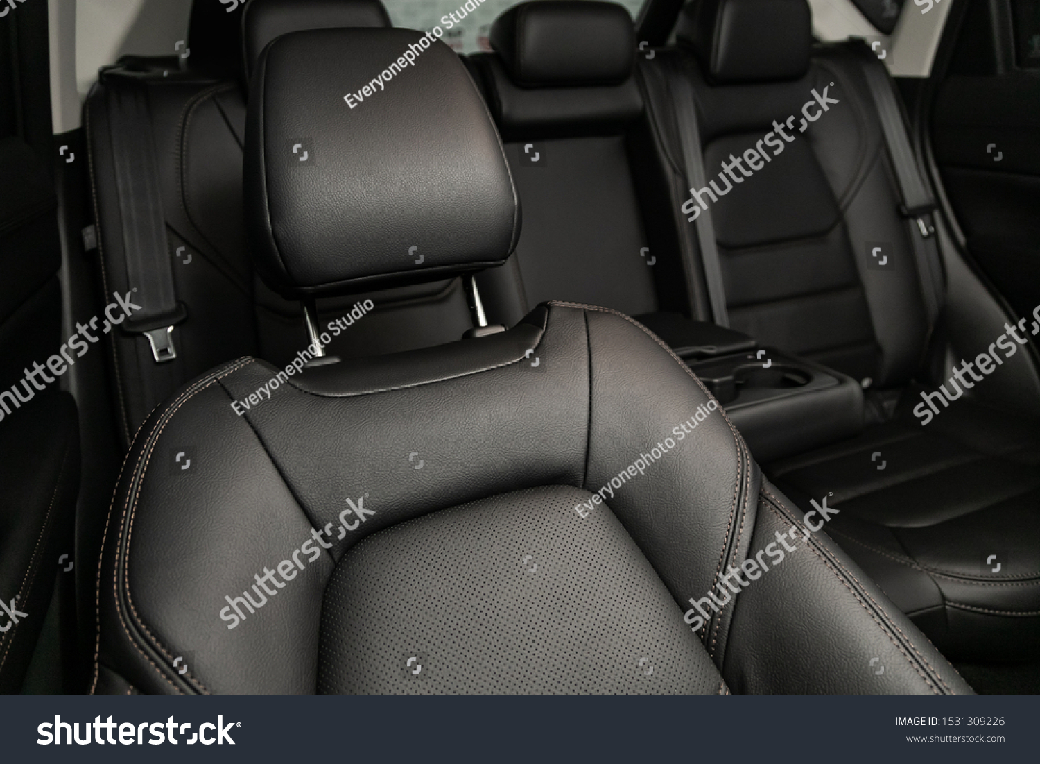 Close-up rear seat made of black leather with a head restraint, in the background passenger seats with seat belts. Luxury car interior #1531309226