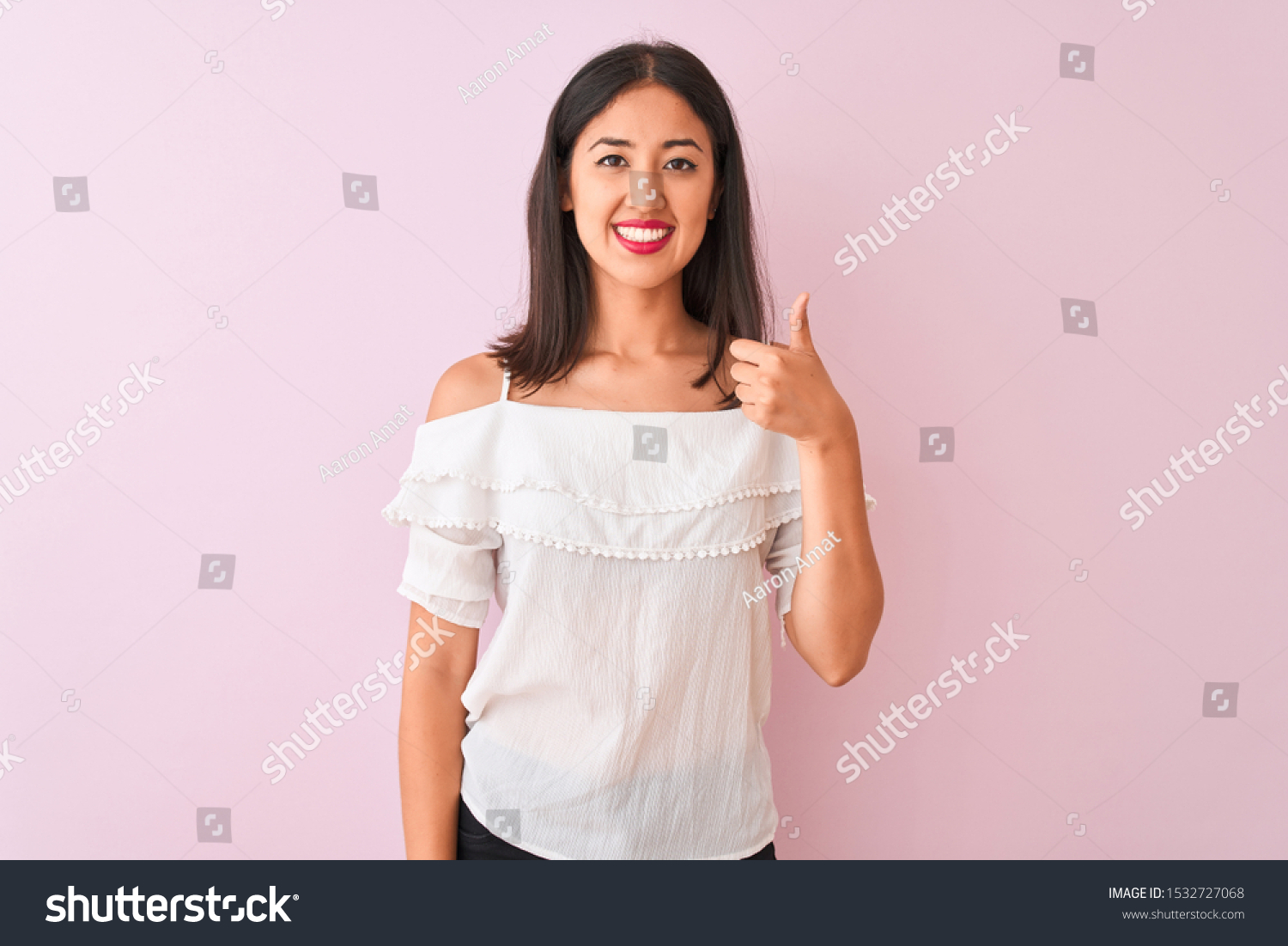 Beautiful chinese woman wearing white t-shirt standing over isolated pink background doing happy thumbs up gesture with hand. Approving expression looking at the camera showing success. #1532727068