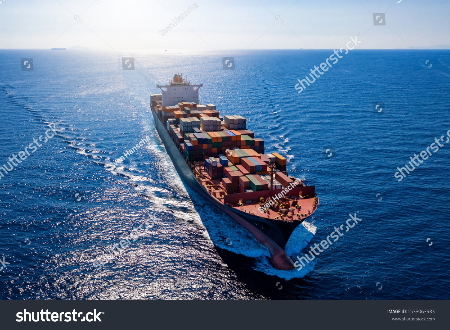 Aerial view of a heavy loaded container cargo vessel traveling in full speed over blue ocean