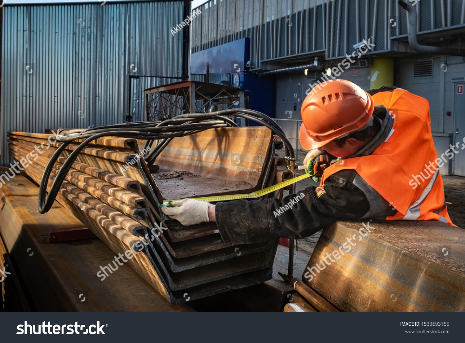 A man measures the size of a sheet pile Larsen. A worker at a construction site in a helmet fulfills his duties of sinking piles and complying with all standards. #1533693155