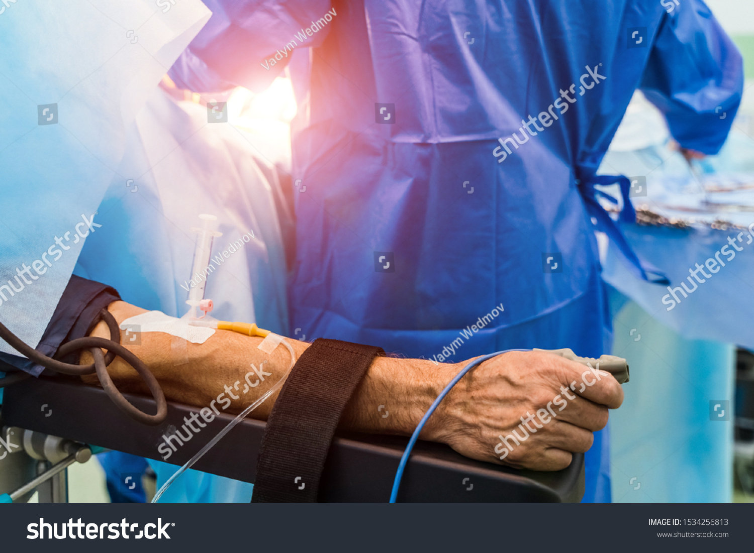 Restrainted patient on the operation table in surgery with a drip in a hand. Patient's hand with a sensor,Hand critically ill patients. IV fluids. Closeup. #1534256813