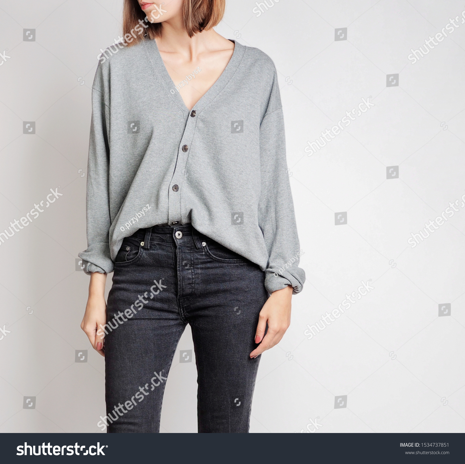 Young woman wearing simple outfit with grey button-up cardigan and black trousers isolated on light grey background. Copy space #1534737851