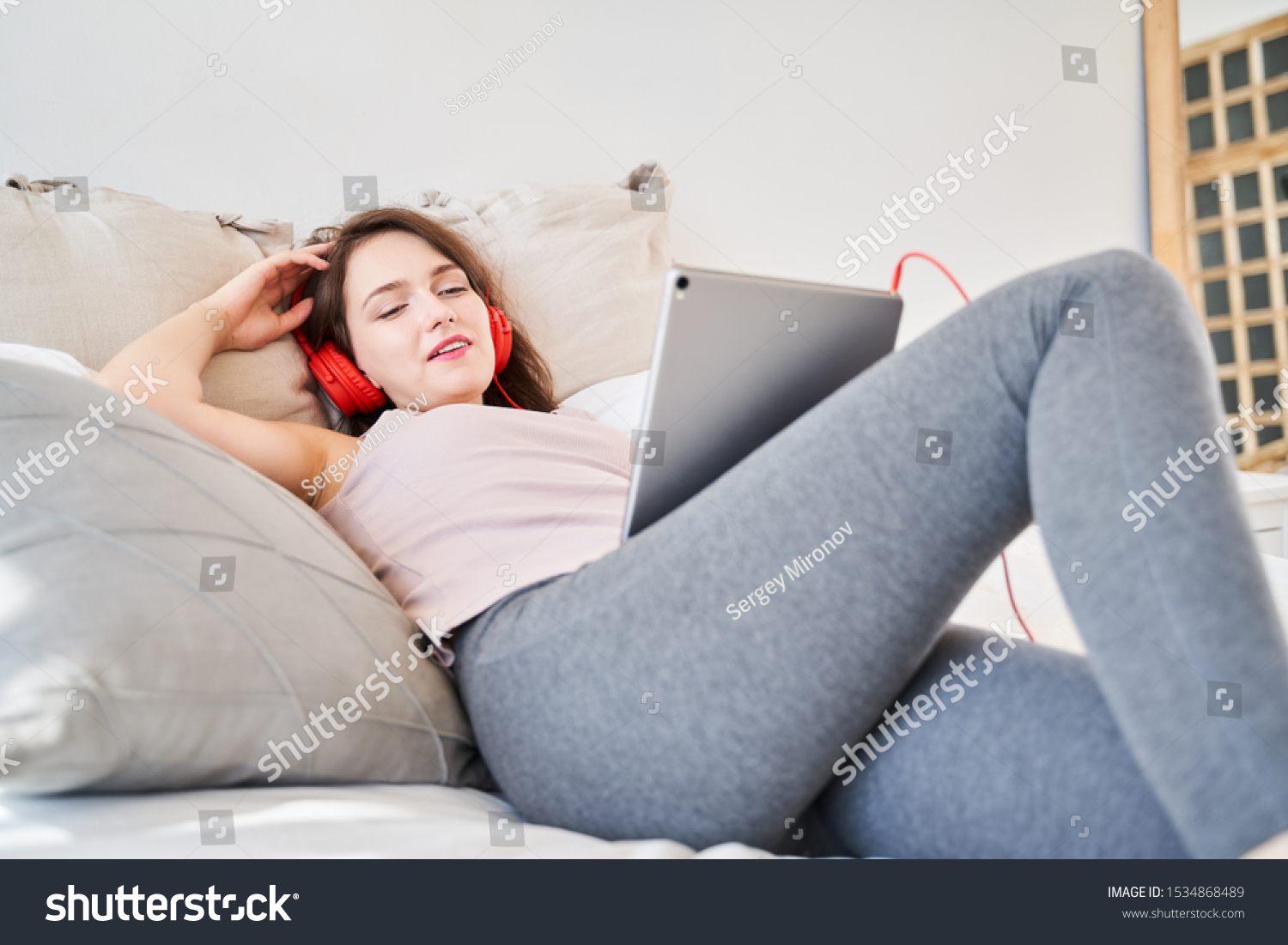 Image of young brunette woman with tablet in her hands listening music while lying on bed. #1534868489