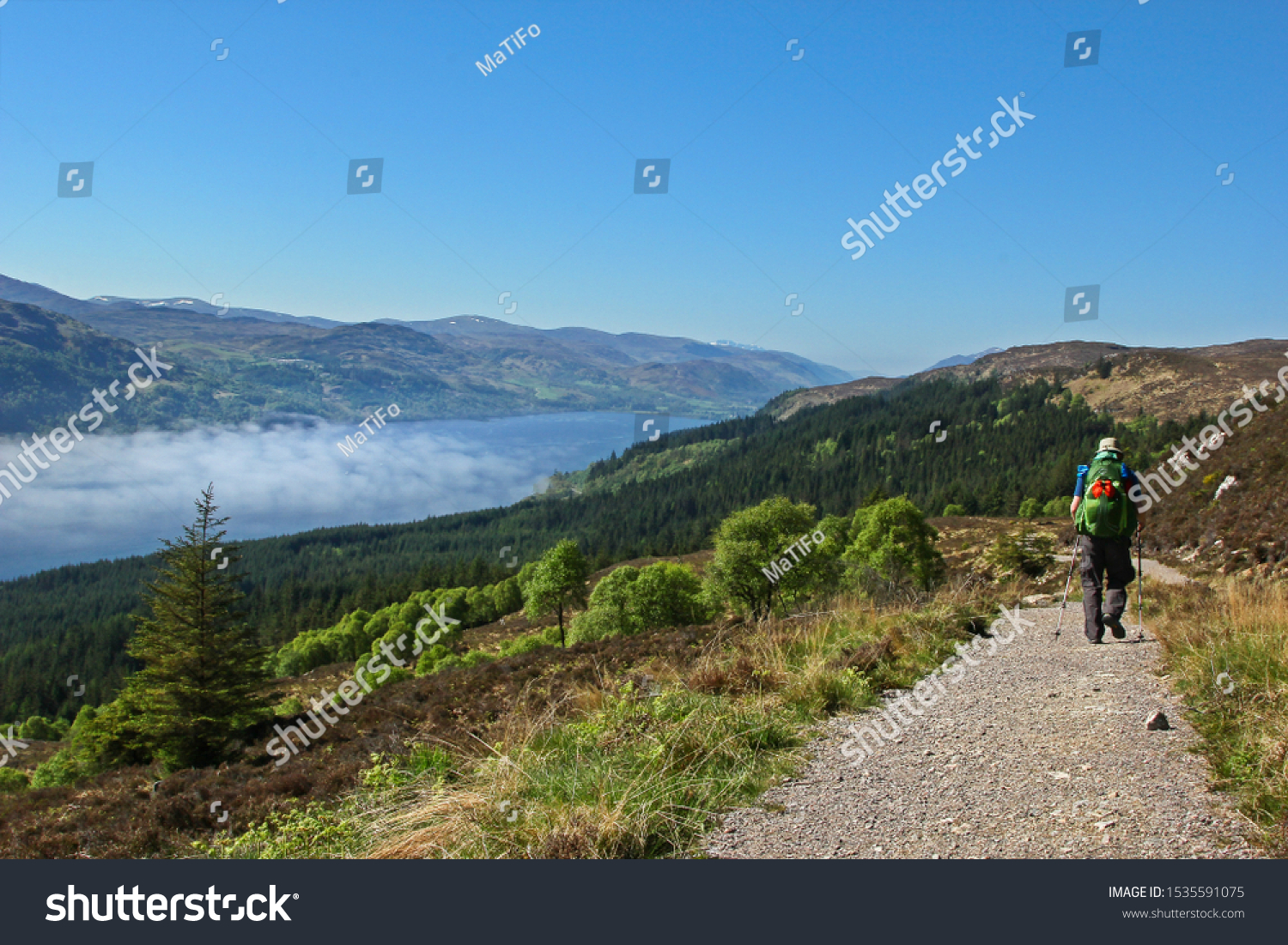 Hiker on the "Great Glen Way" in Scotland, with Scottish highlands and loch in the distance #1535591075