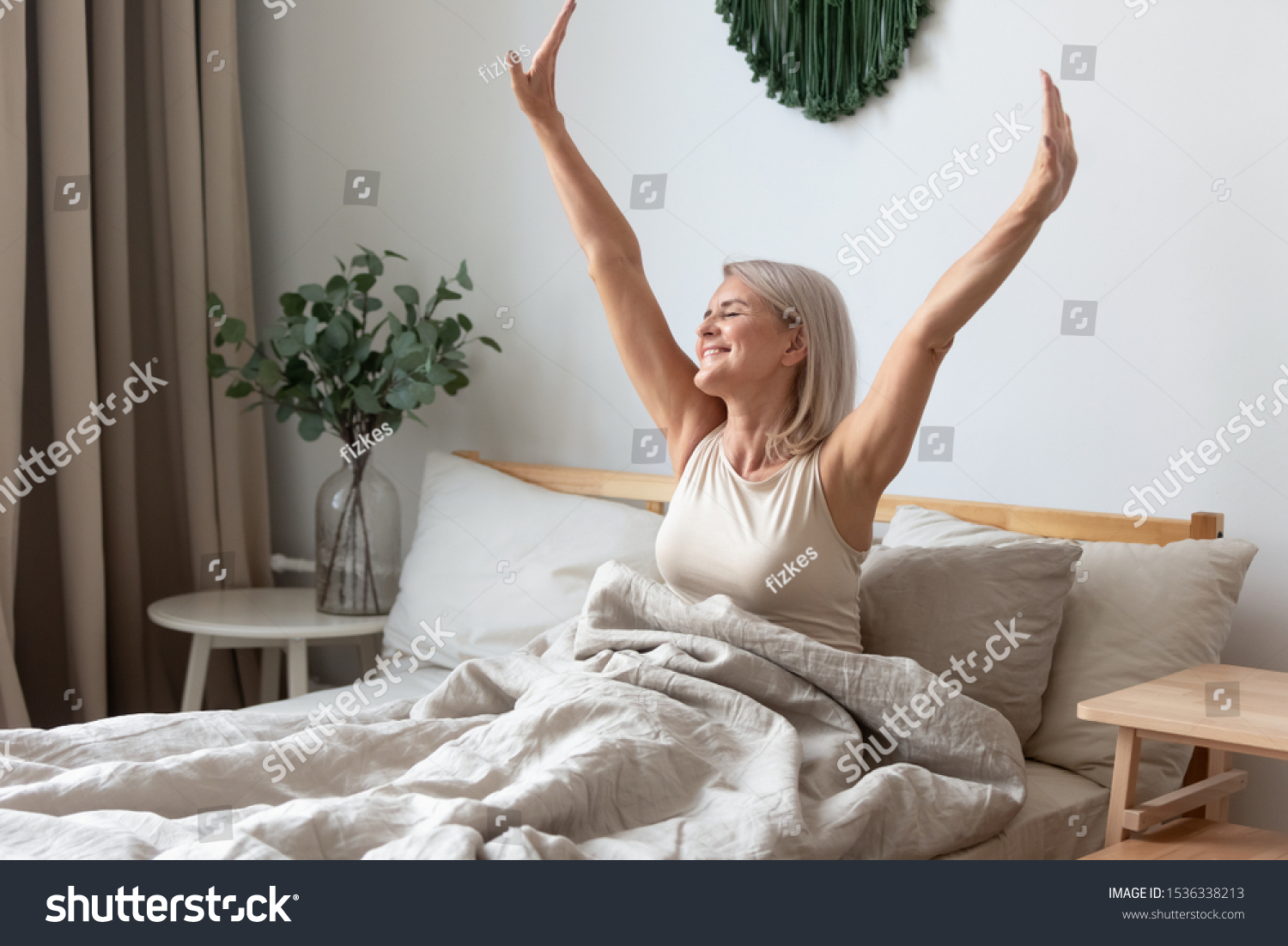 Happy fresh mature middle aged woman stretching in bed waking up alone happy concept, smiling old senior lady awake after healthy sleep sitting in cozy comfortable bedroom interior enjoy good morning #1536338213