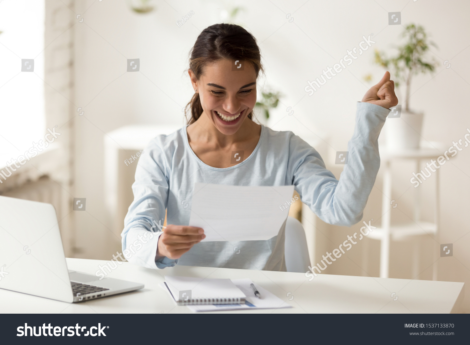 Overjoyed millennial mixed race female worker employee reading letter with good news, celebrating special achievement. Smiling young woman getting bank loan approval or lottery win notification. #1537133870