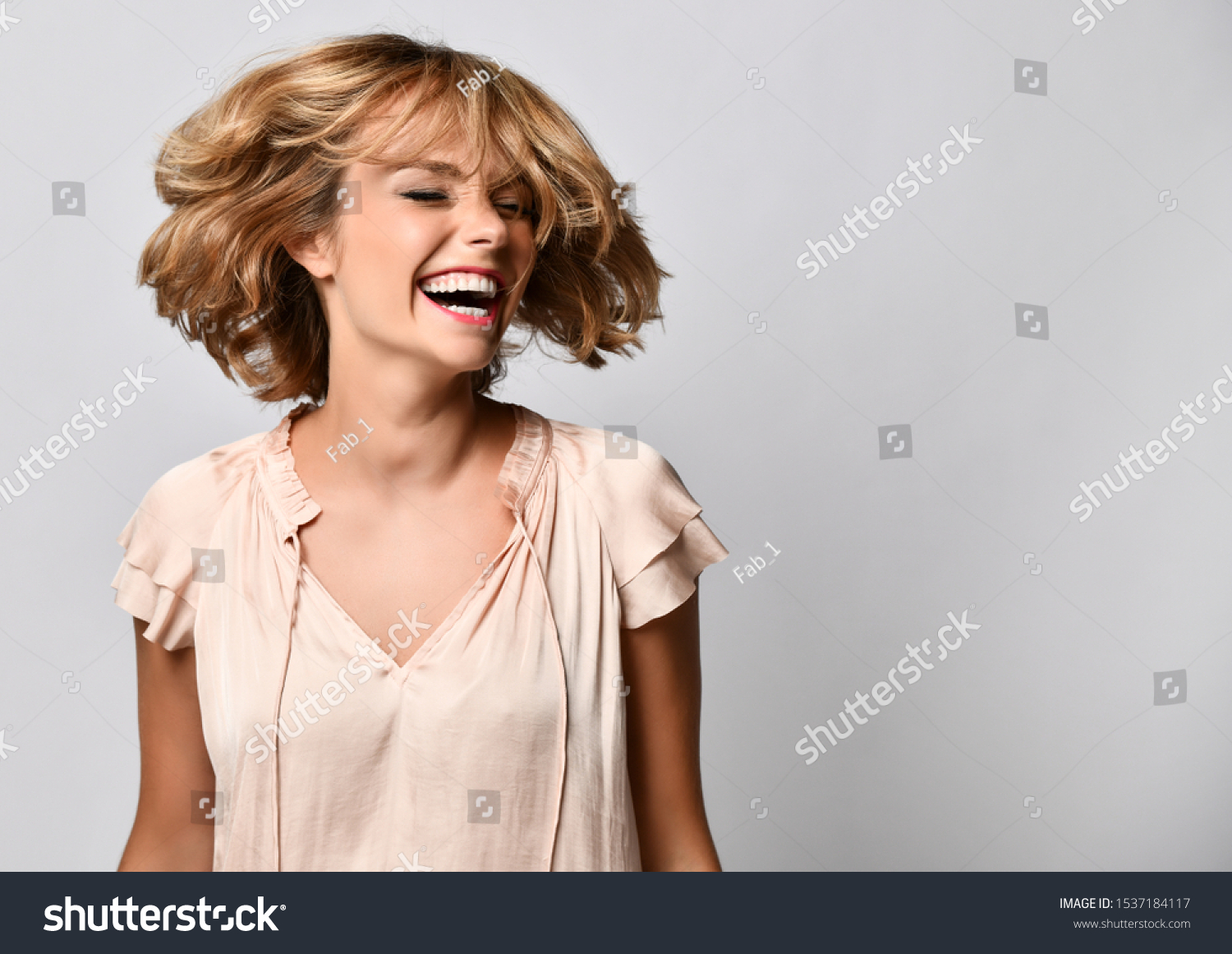 young woman in a beige short-sleeved satin blouse shakes her head with her hair. The concept of joy, happiness, joy, fun #1537184117