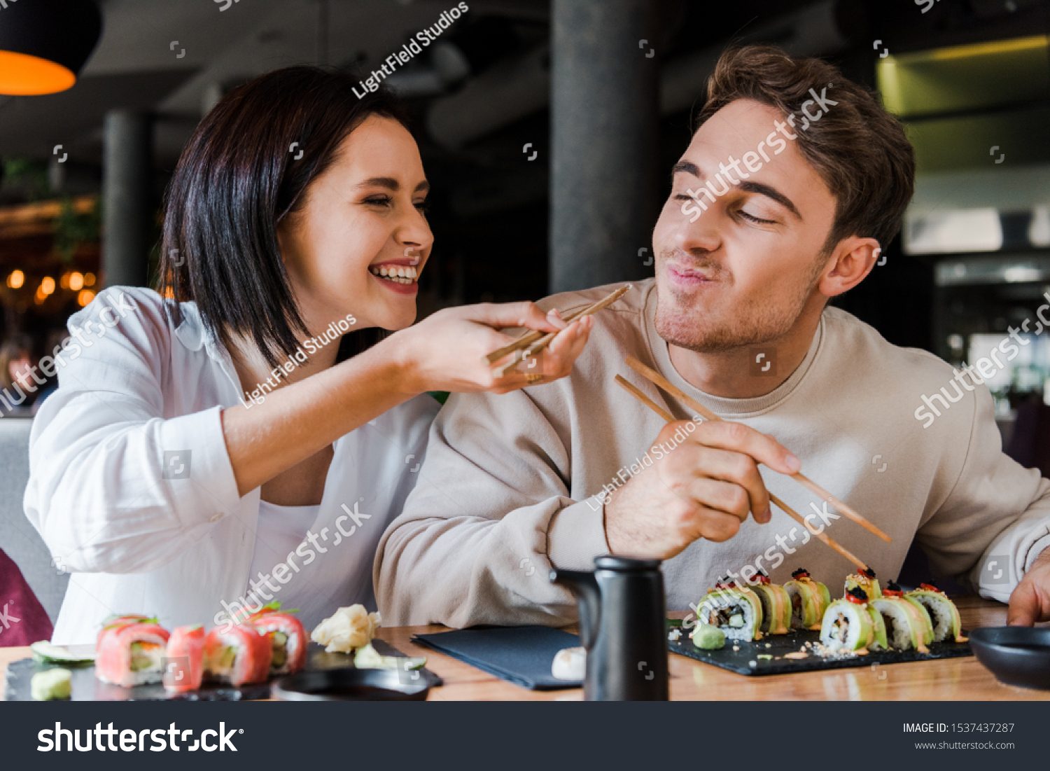 selective focus of happy woman holding chopsticks with tasty sushi near cheerful man in restaurant  #1537437287