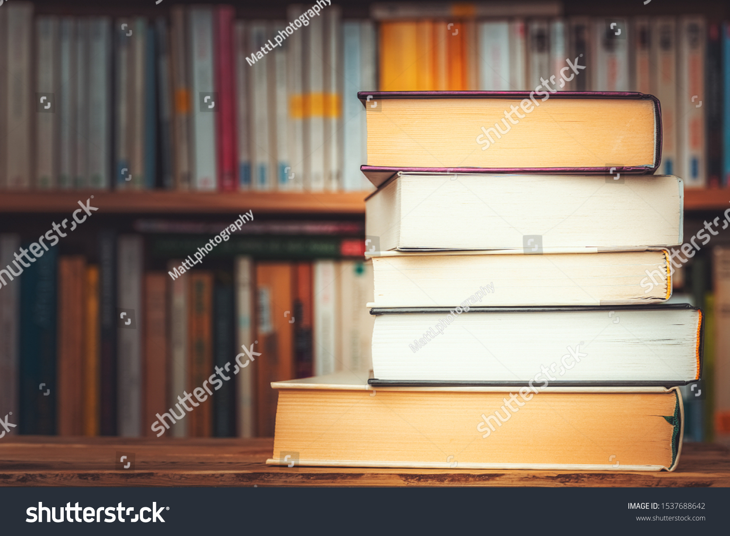 Pile of big books with blurry bookshelf in the background and copy space. Knowledge, reading, study, literacy or literature illustrative concept. #1537688642