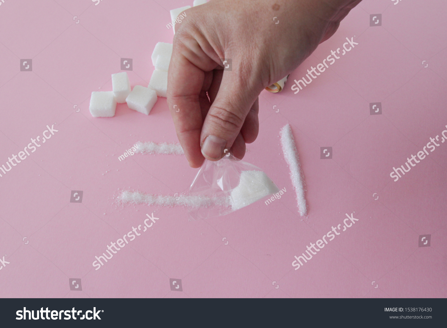 Hand of a woman with a pack of sugar like it was drug on pink background #1538176430