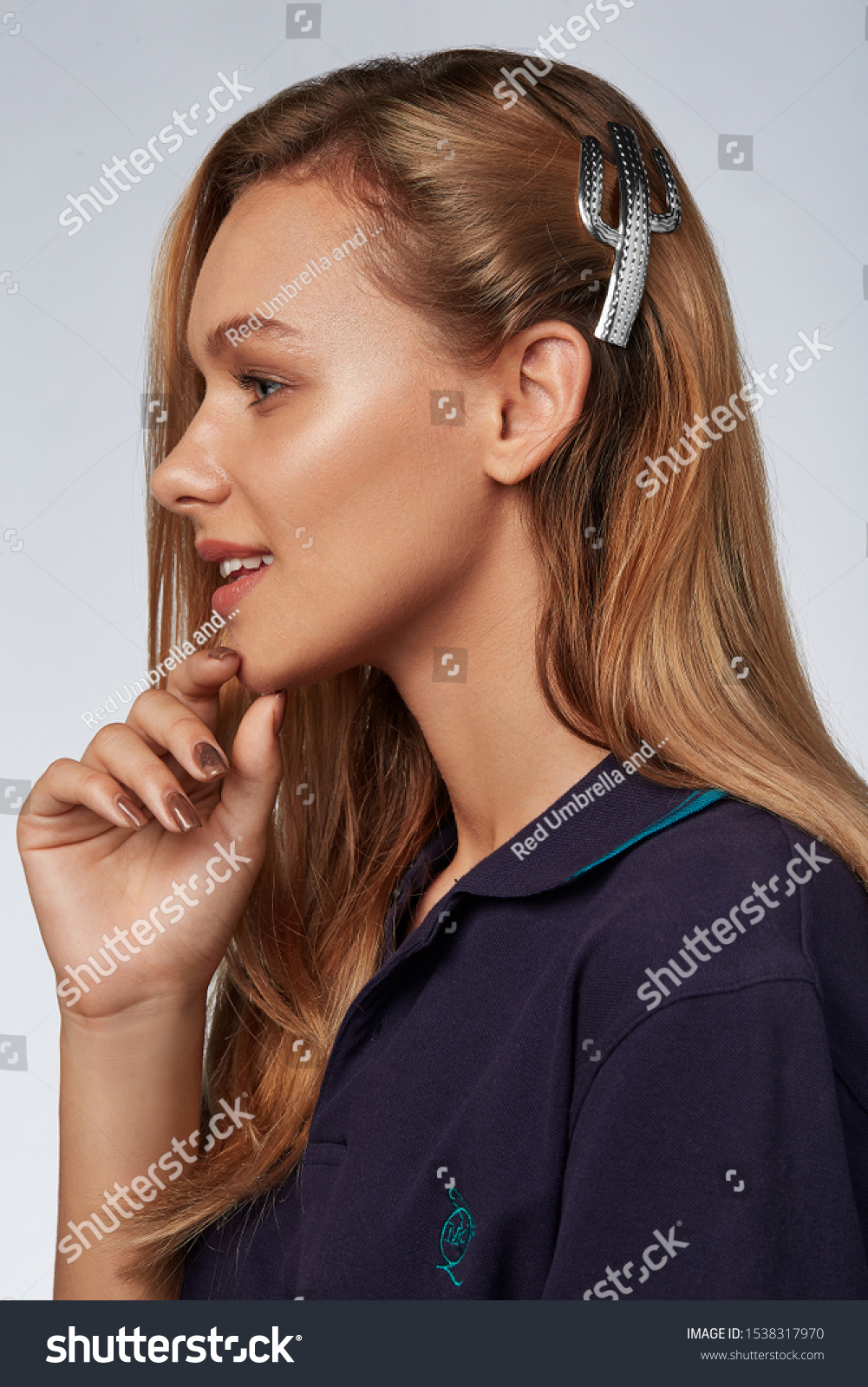  Profile portrait shot of a smiling lady with blond hair, posing on a blue background. She has a silver hair clip in the form of cactus. The girl is wearing a dark blue T-shirt #1538317970