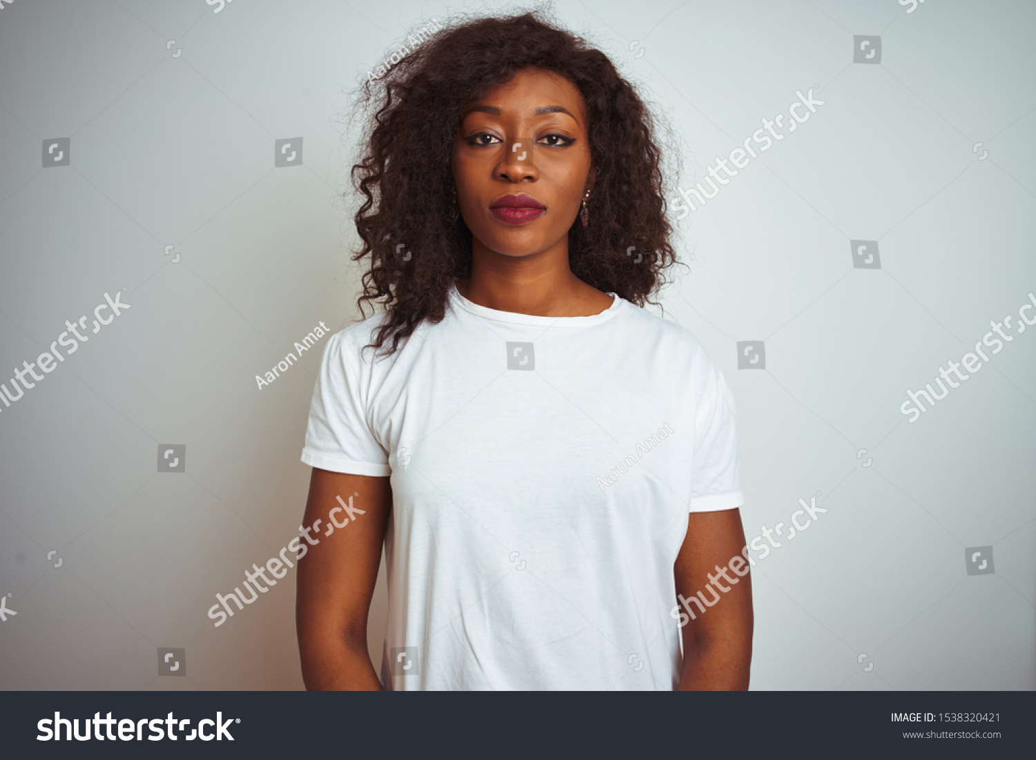 Young african american woman wearing t-shirt standing over isolated white background Relaxed with serious expression on face. Simple and natural looking at the camera. #1538320421