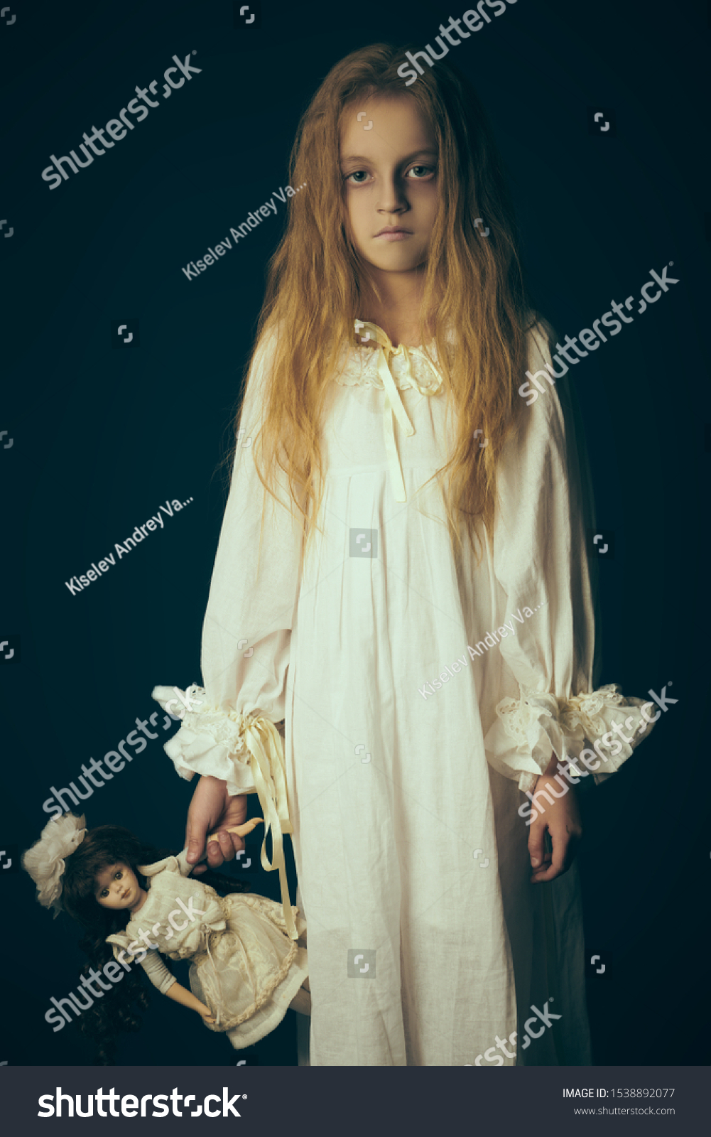 Scary little girl ghost in a white nightgown holds her doll. Black background. Halloween.  #1538892077