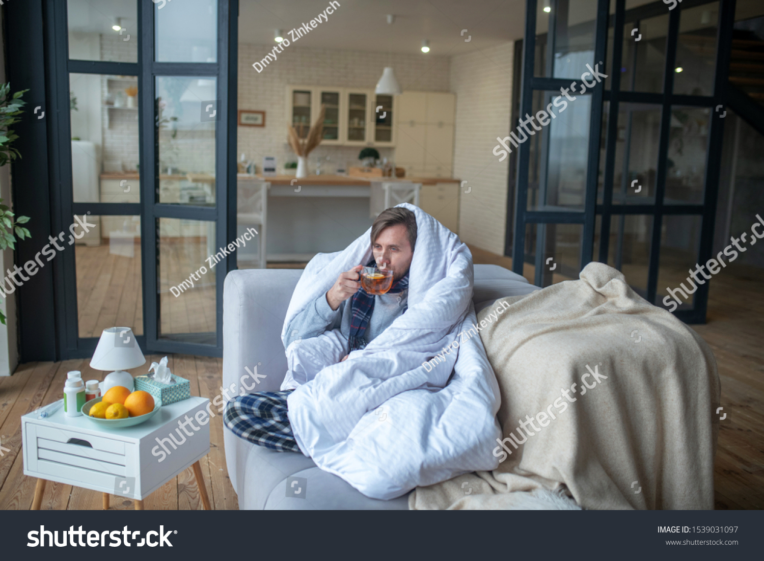 Man feeling cold. Man feeling cold so drinking hot tea and covering in bedsheet in living room #1539031097