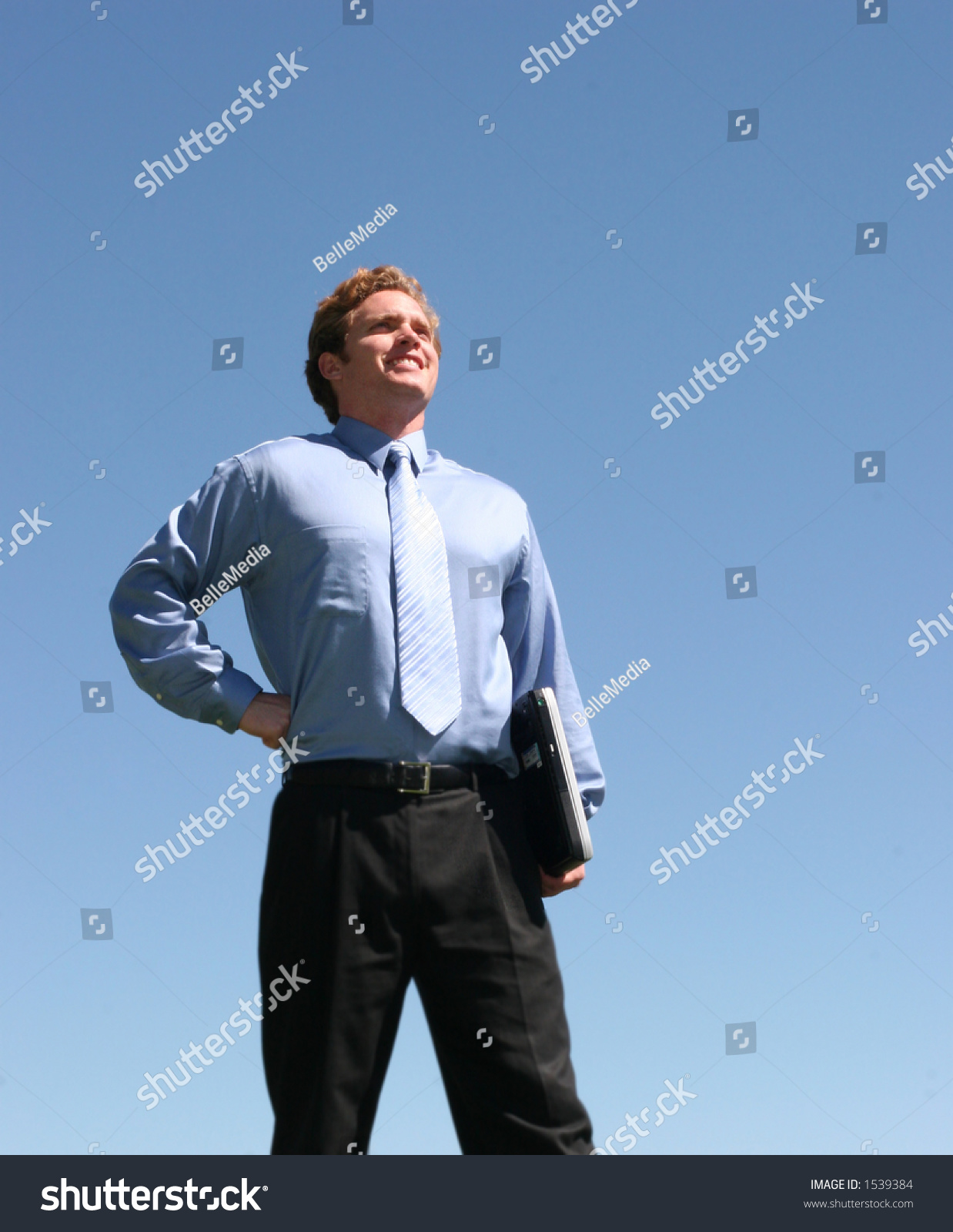 Business man in blue shirt and blue tie, holding laptop against blue sky #1539384