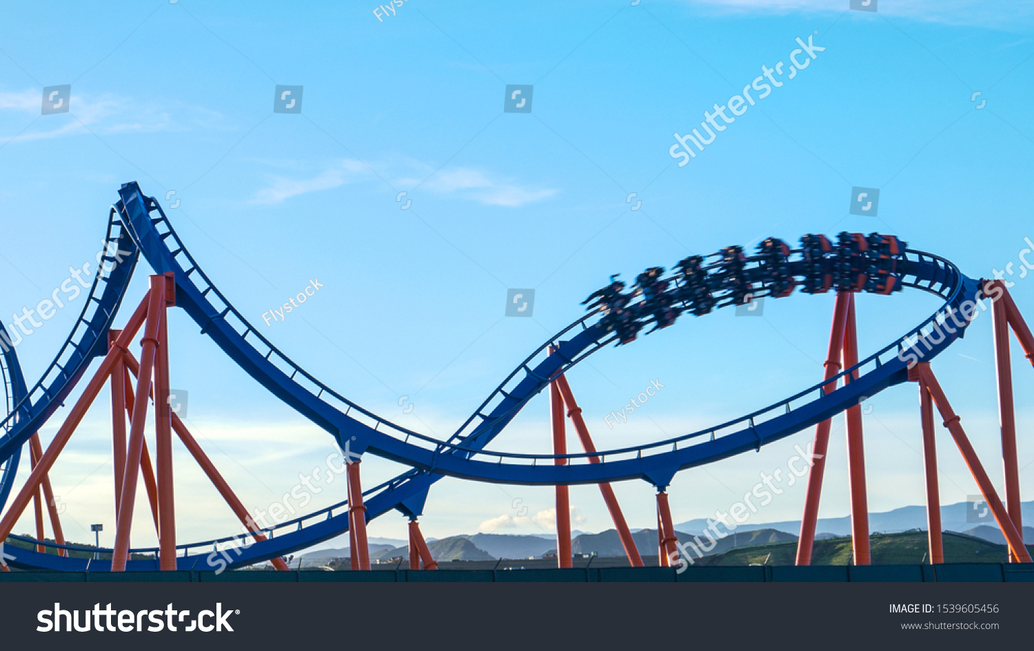 CLOSE UP: Excited tourists are thrown around as the ride the epic roller coaster speeding into a sharp turn. Thrill-seeking tourists ride the fun roller coasters in an amusement park in Los Angeles. #1539605456