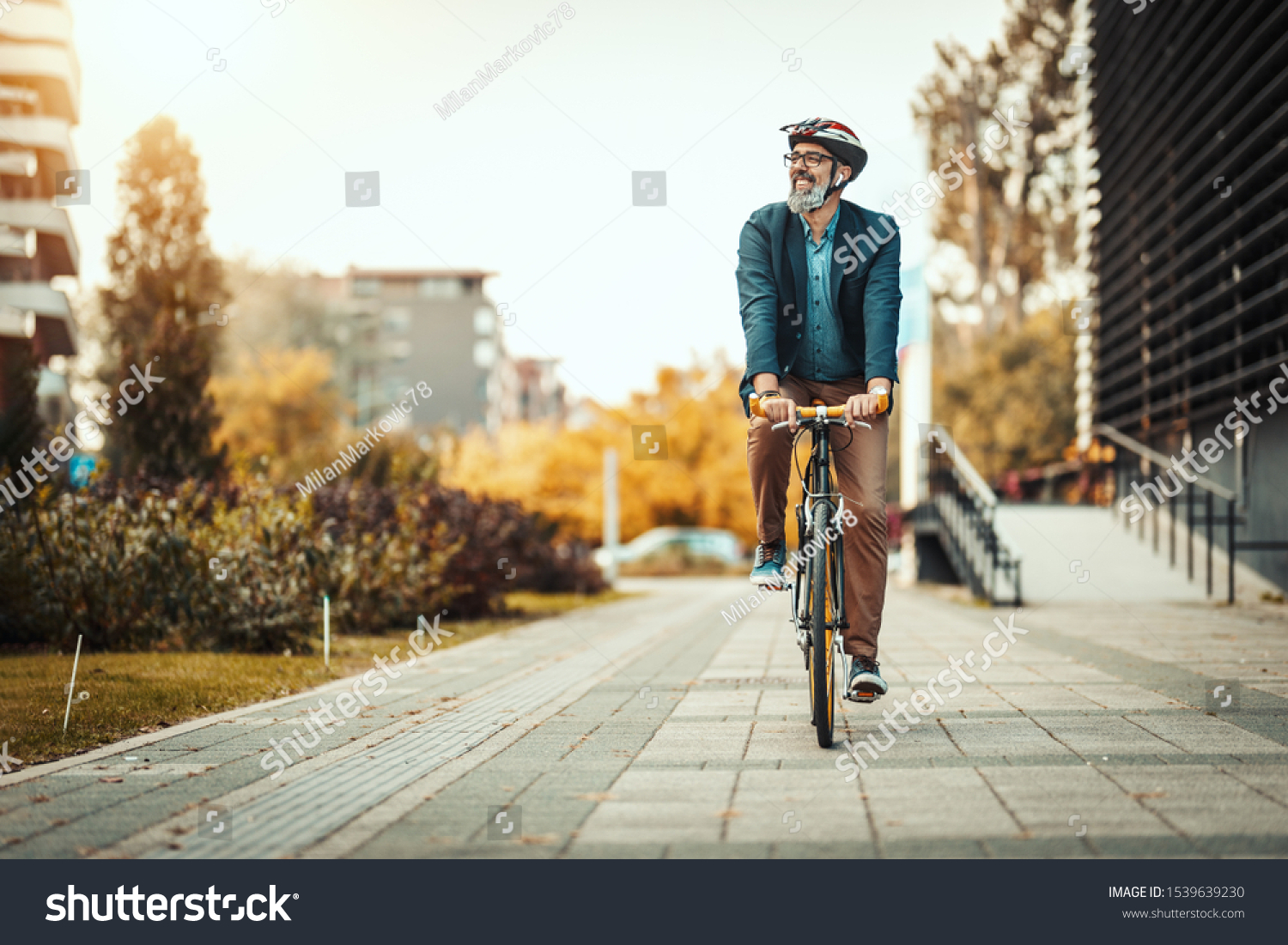 A handsome casual middle-aged businessman is going to the office by bicycle. He is driving bike in front of office district. #1539639230
