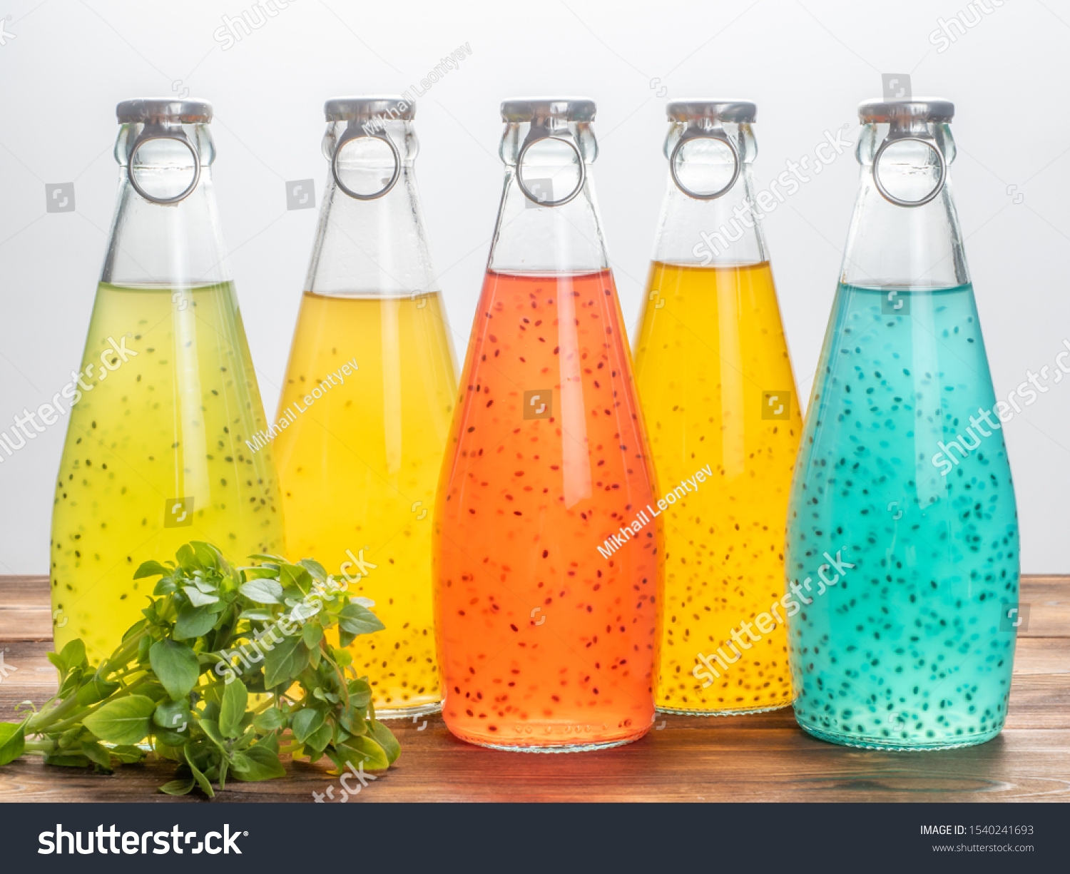 Five bottles of Basil Seed on a white background with basil leaves. Red, yellow, light blue and green color. Soft focus. #1540241693