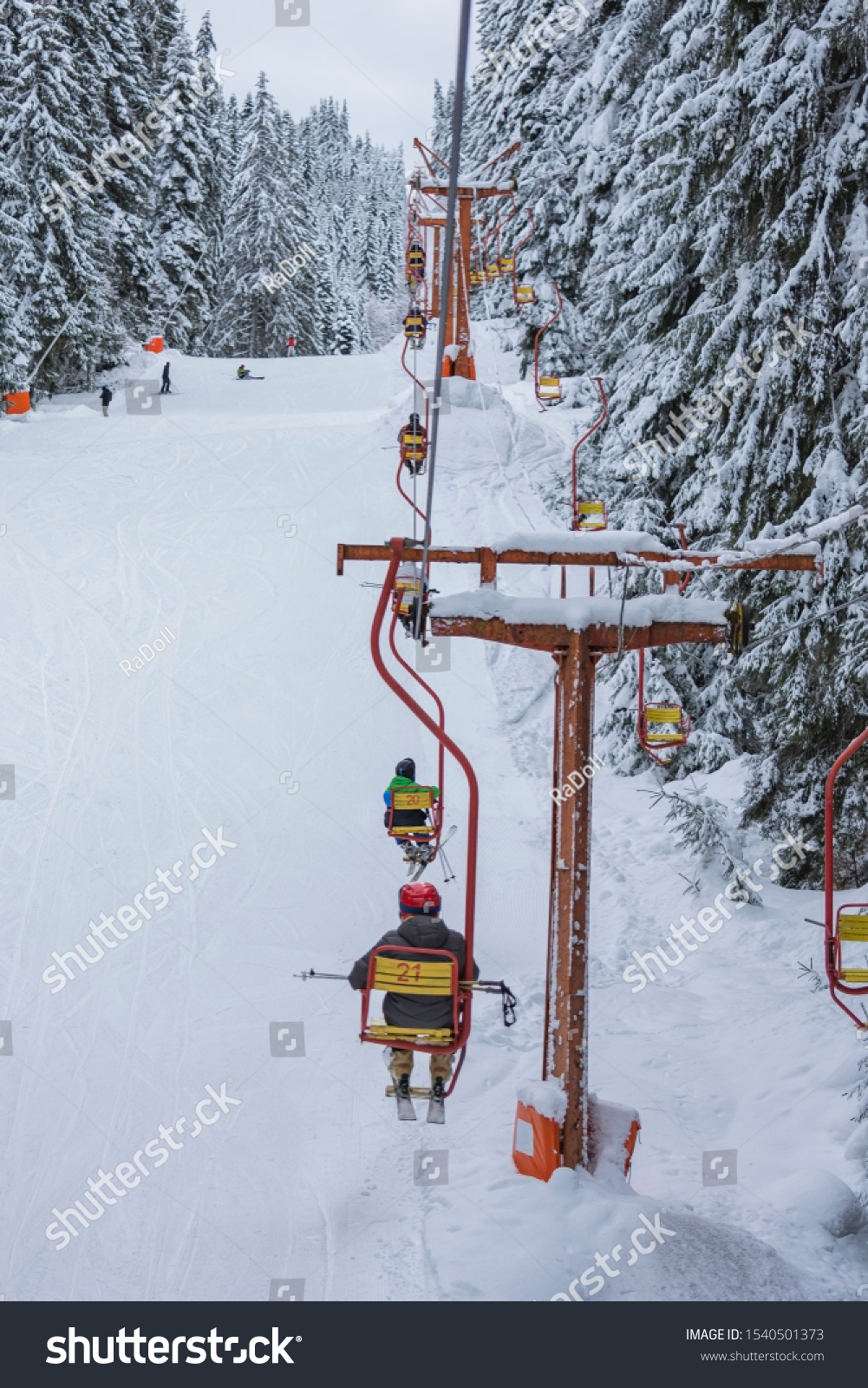 Chair ski lift next to slope for skis and snowboards. Skiers are sitting at old fashioned chair ski lift. Ski area in snowy high mountain. Sports and recreation concept. Selective focus. #1540501373