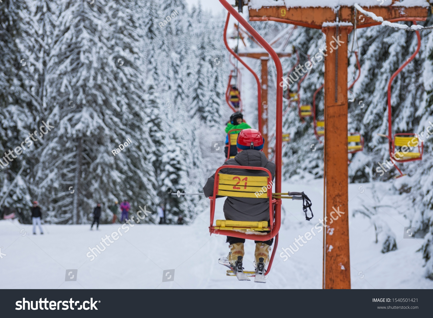 Skiers are sitting at old fashioned one chair ski lift.  Chair ski lift next to slope for skis and snowboards.  Ski area in snowy high mountain. Sports and recreation concept. Selective focus. #1540501421