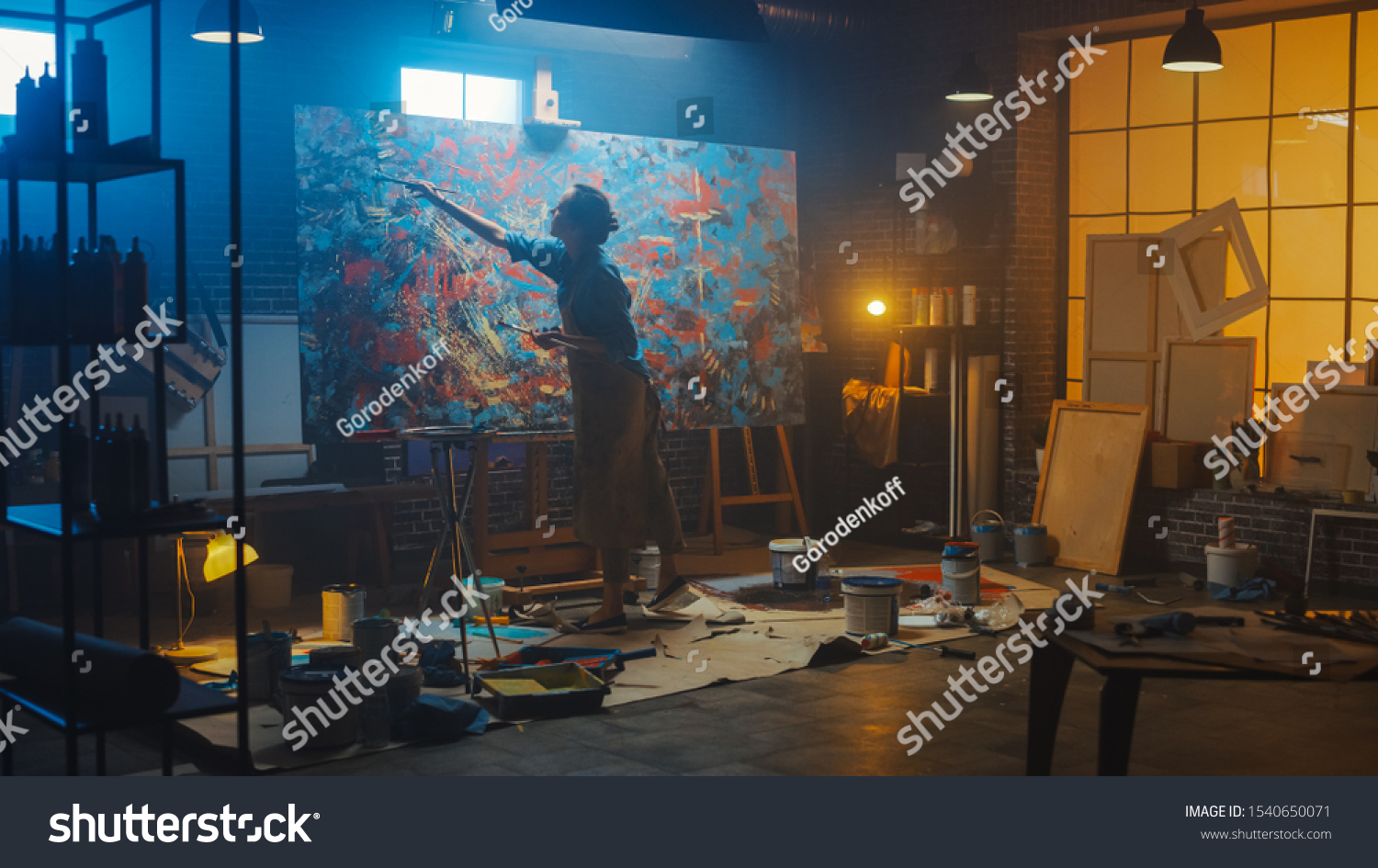 Talented Female Artist Works on Abstract Oil Painting, Using Paint Brush She Creates Modern Masterpiece. Dark and Messy Creative Studio where Large Canvas Stands on Easel Illuminated #1540650071