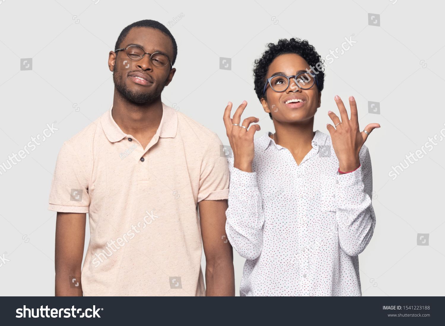 Head shot bored African American man listening to excited smiling woman, bad conversation, beautiful girlfriend talking to boyfriend, friends wearing glasses standing isolated on grey background #1541223188