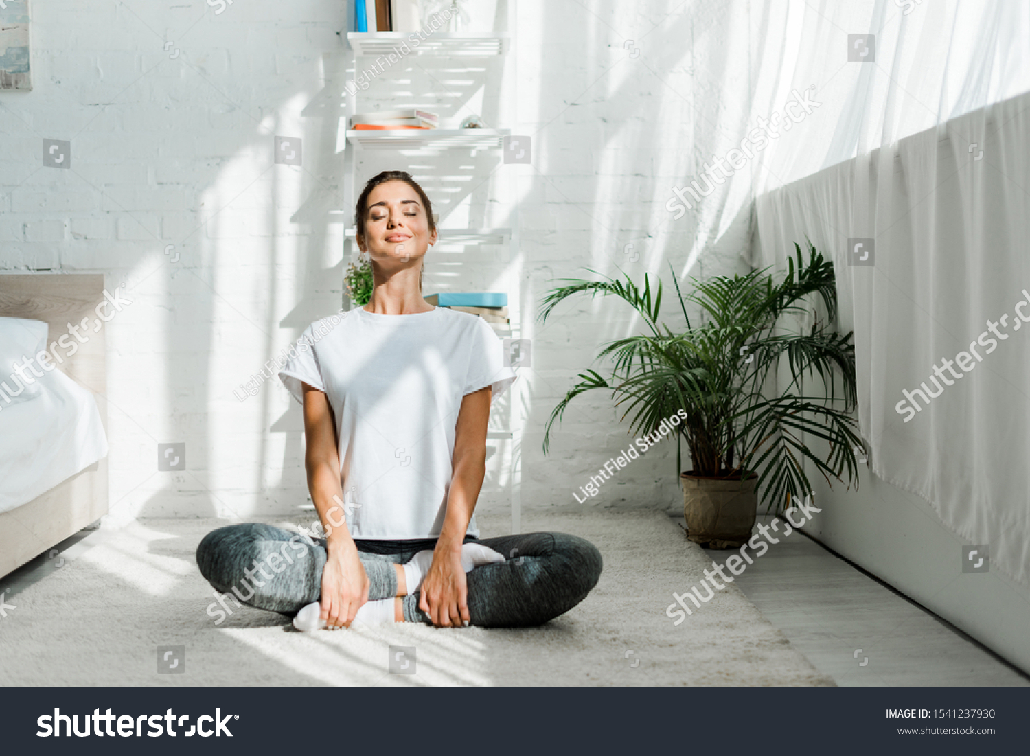 beautiful happy girl with closed eyes practicing yoga in lotus position in bedroom in the morning  #1541237930