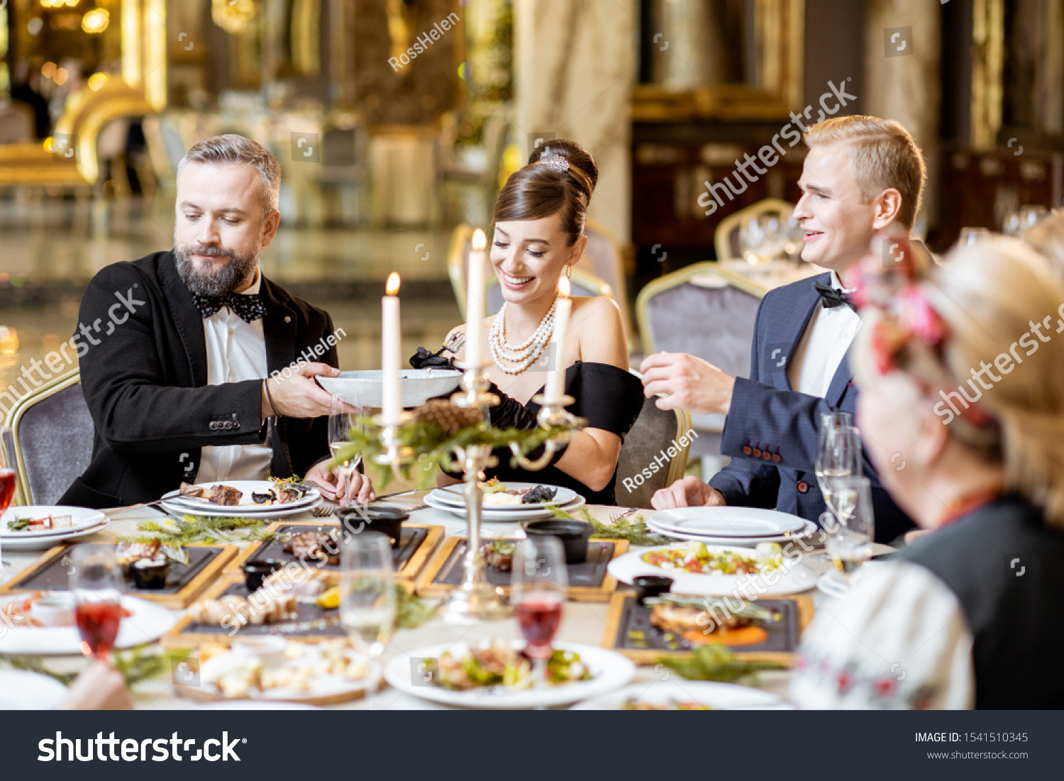 Elegantly dressed group of people having a festive dinner at a well-served table with tasty dishes during New Year Eve at the luxury restaurant #1541510345