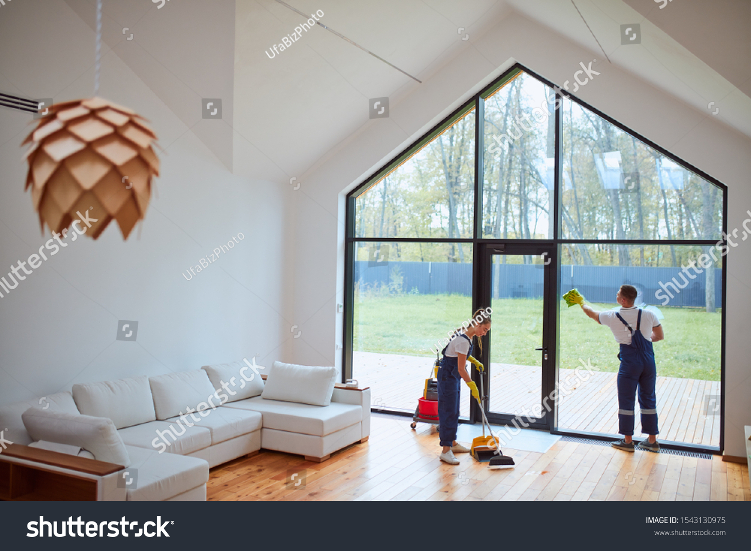 Preparing house for new tenant. Cleaning service washing floor, window. Man cleaning panoramic window with view on garden. Woman sweeping the floor #1543130975