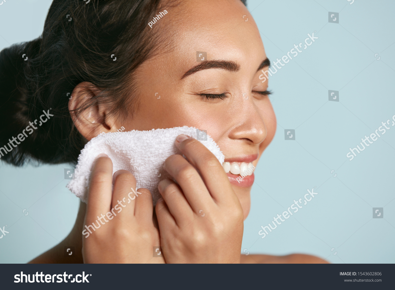 Woman cleaning facial skin with towel after washing face portrait. Beautiful happy smiling young asian female model wiping facial skin with soft towel, removing makeup. High quality studio shot #1543602806