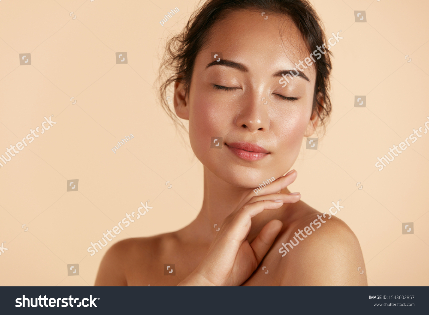 Beauty face. Woman with natural makeup and healthy skin portrait. Beautiful asian girl model touching fresh glowing hydrated facial skin on beige background closeup. Skin care concept #1543602857