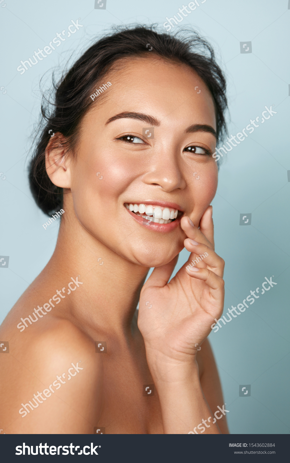 Beauty face. Smiling asian woman touching healthy skin portrait. Beautiful happy girl model with fresh glowing hydrated facial skin and natural makeup on blue background at studio. Skin care concept #1543602884