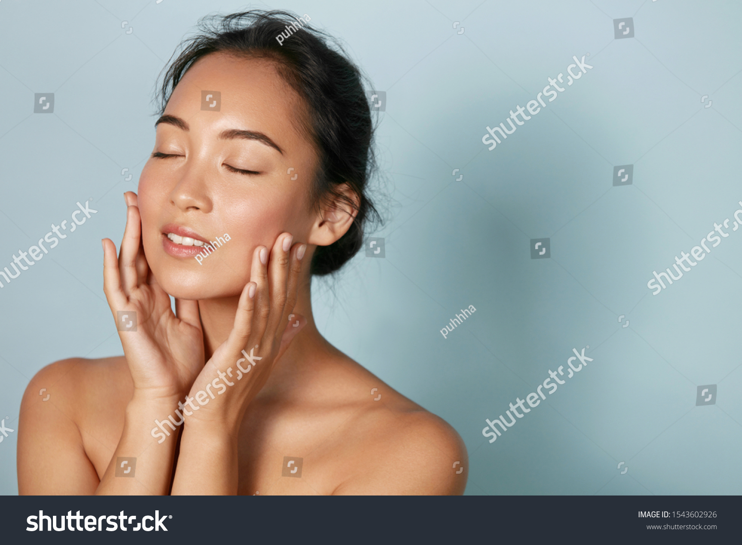 Skin care. Woman with beauty face and healthy facial skin portrait. Beautiful asian girl model with natural makeup touching glowing hydrated skin on blue background closeup. High quality image
