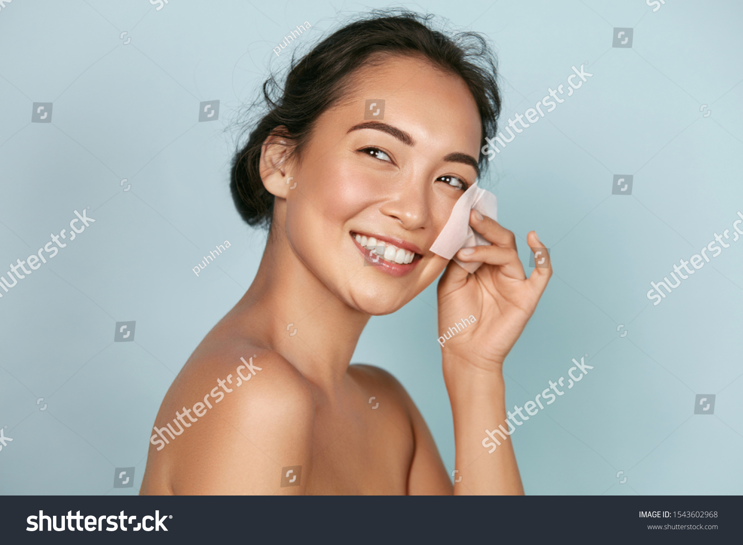 Face skin care. Smiling woman using facial oil blotting paper portrait. Closeup of beautiful happy asian girl model with natural makeup using oil absorbing sheets, beauty product at studio #1543602968