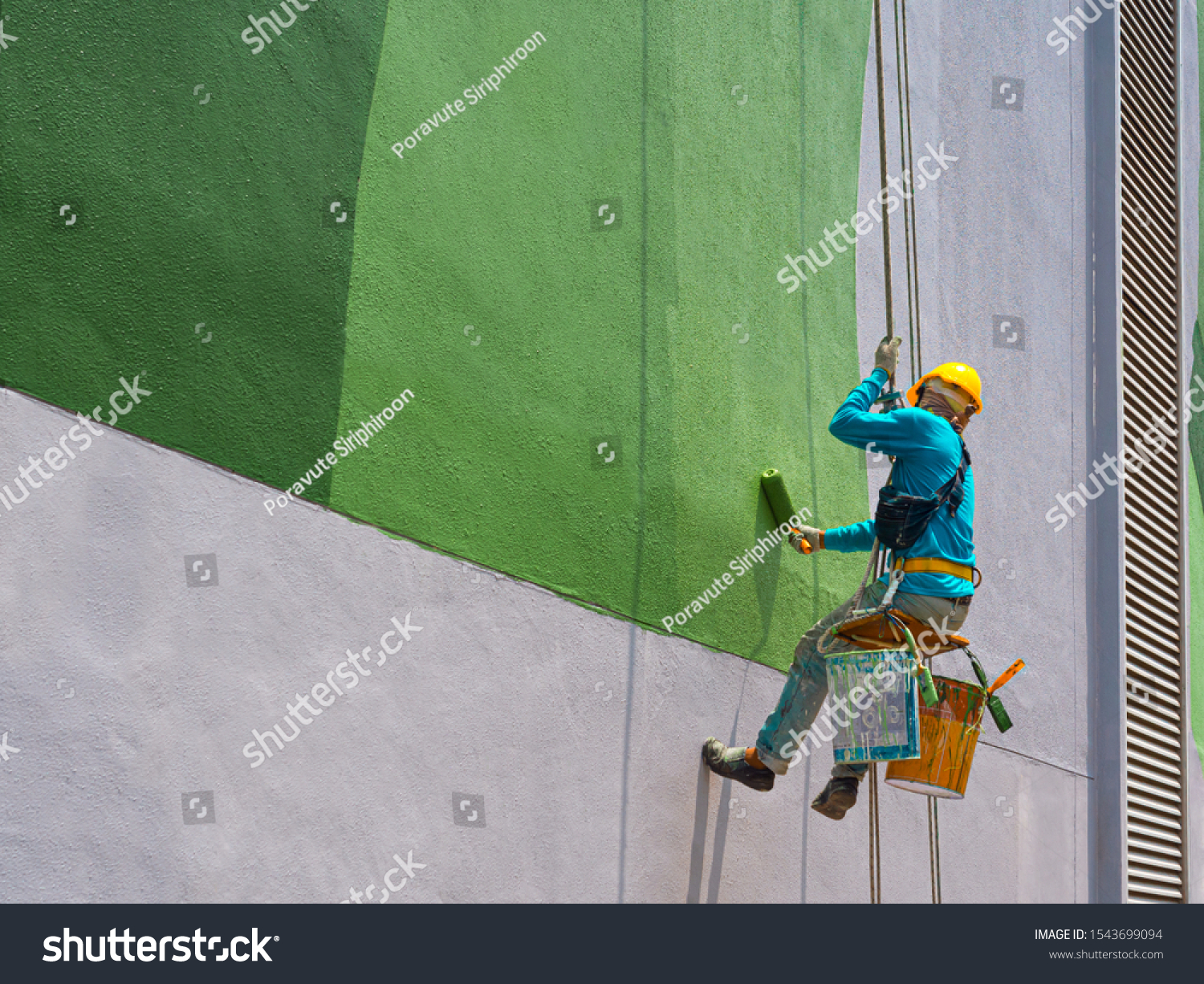 One painter is painting the exterior of the building on a dangerous looking scaffolding hanging from a tall building. #1543699094